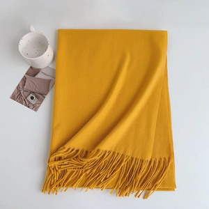 Close-up of soft ginger yellow cashmere scarf with tassels and decorative ceramic cup