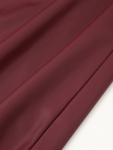 Gros plan de la texture du cuir synthétique rouge foncé avec plis et fini brillant