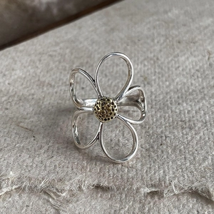 Silver daisy open ring with gold floral center on minimalist textured gray background