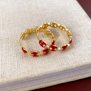 Detail of 18k gold plated earrings with red enamel and pavé zircon on a linen surface