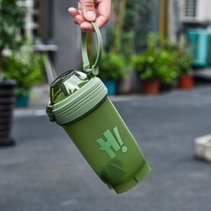 Green portable shaker bottle with carrying handle and mixing ball in outdoor setting