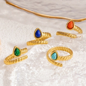 Macro detail of four gold spiral rings with teardrop natural stones on a glass plate