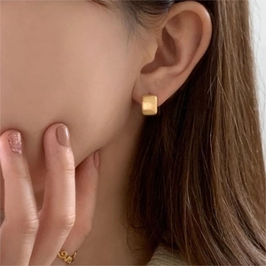 Close-up of golden matte square stud earrings on female ear with warm lighting