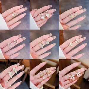 Multiple styles of gold stud earrings with pearls and heart shapes held by a hand
