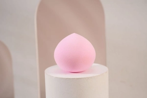 Close-up of a soft pink teardrop-shaped makeup sponge on a minimalist geometric background