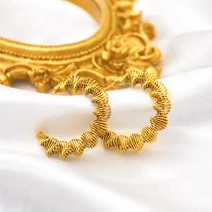 Macro detail of 18k gold plated spring hoop earrings on a luxury white silk background