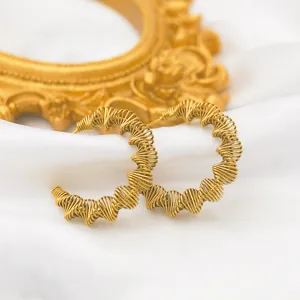Macro detail of 18k gold plated spring hoop earrings on a luxury white silk background