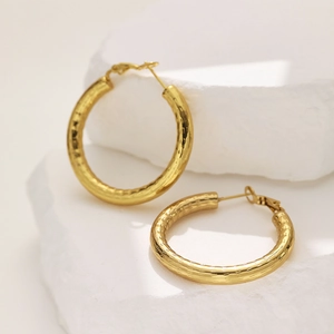 Close-up of golden hollow hoop earrings with hammered texture on white stone
