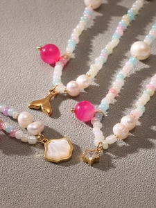 Detailed macro view of pastel beaded necklace with pearls and golden fish tail charms
