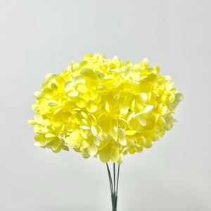 Detailed view of vibrant yellow artificial hydrangea petals and green stems on a neutral wall