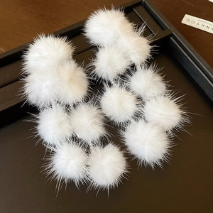 Macro shot of soft white plush pom-pom earrings on a black tray with a wooden backdrop