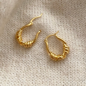Detail of gold twisted rope U-shaped hoop earrings on soft cream knit fabric