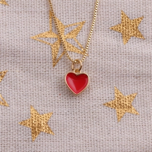 Close-up of golden chain necklace featuring a red enamel heart pendant on star fabric