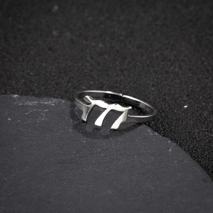 Macro shot of adjustable silver number 77 ring on dark textured stone surface