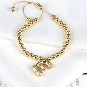 Detail of adjustable gold bead bracelet featuring a sparkling zircon initial E charm