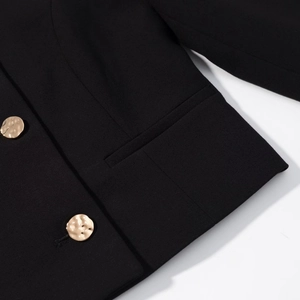 Dettaglio ravvicinato di un blazer nero con bottoni in metallo martellato dorato e tasca
