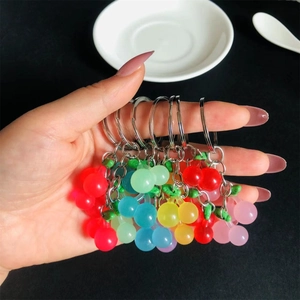 Hand holding colorful resin cherry keychains in red pink yellow and blue hues
