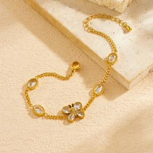 Gold butterfly charm bracelet with oval zircon accents on a textured sand surface