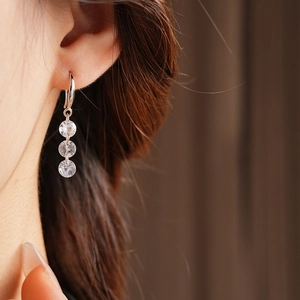 Close-up of minimalist silver tassel earrings with three sparkling zircons on a model