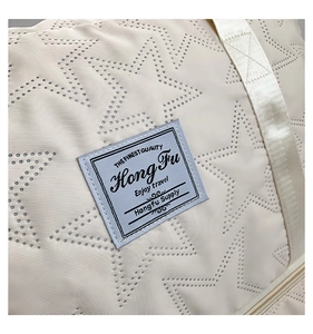 Close-up of star-patterned laser-cut fabric and brand label on cream travel bag