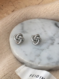 Elegant knot stud earrings in silver on white marble and beige knit background