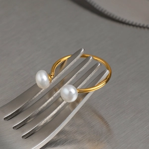 Dettaglio ravvicinato di un anello aperto placcato oro con due perle su metallo