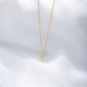 Macro detail of minimalist gold lightning bolt pendant on a white satin background