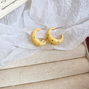 Detail of yellow C-shaped earrings with blue speckled pattern and gold-tone posts
