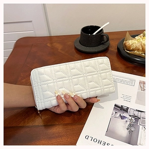 Detailed view of white quilted long wallet with gold zipper on a lifestyle background