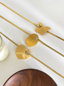 Detailed shot of gold snake chains with butterfly, oval and heart pendants on white surface