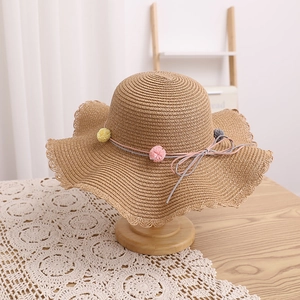 Detail of children's straw hat with wavy brim, colorful pom-poms, and light woven texture