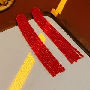 Close-up of red rhinestone fringe earrings with light effects on beige fabric