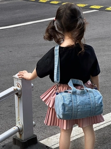 Kids blue denim cylinder crossbody bag shown on child model in outdoor street setting