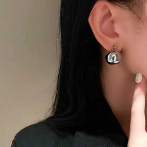 Close-up of a model wearing minimalist silver spherical metal earrings in a French retro style