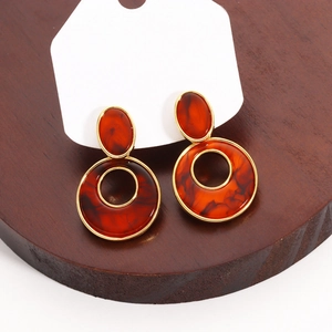 Detail view of amber resin and gold geometric hollow earrings on a wooden stand