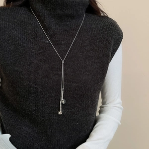 Detail view of long silver sweater chain with geometric pendant on a grey turtleneck