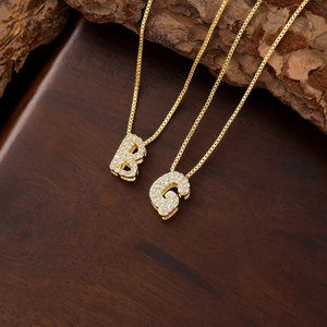 Detail view of gold bubble letters B and S pendants with sparkling cubic zirconia inlay