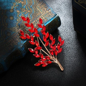 Detail shot of a wheat-shaped brooch with red crystals on a textured dark background