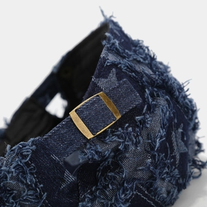 Macro detail of dark blue denim hat featuring frayed edges and star patterned fabric texture