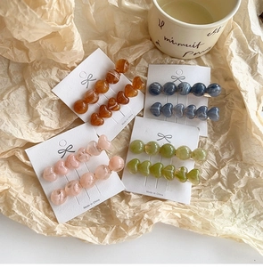 Detail of four colorful resin heart hair clips on display card with marble textures