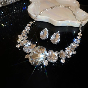 Detailed close-up of sparkling silver teardrop necklace and earrings set on black background