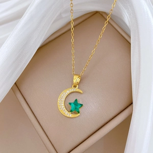 Detail of gold necklace with crescent moon and green star pendants on beige jewelry box