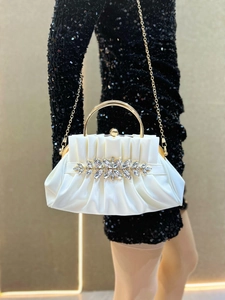 Detailed macro view of white pleated clutch bag with golden metal handle and crystal flower