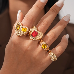 Close-up of four vintage gold rings with textured metal and red gemstones worn by a model