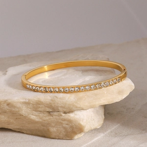 Elegant gold stainless steel bangle with single row of clear zircons on a natural stone