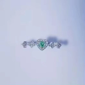 Macro detail of silver ring featuring heart-shaped green emerald and micro-pave diamonds
