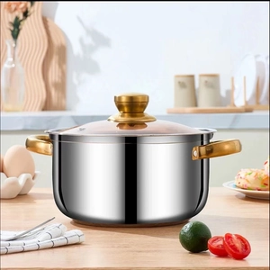 Golden double-handled stainless steel soup pot with glass lid on a wooden table