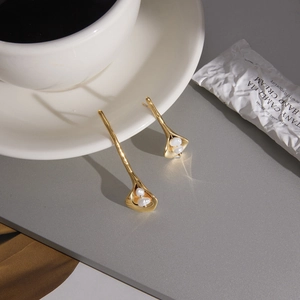 Elegant gold calla lily pearl earrings on a marble surface with artistic lighting