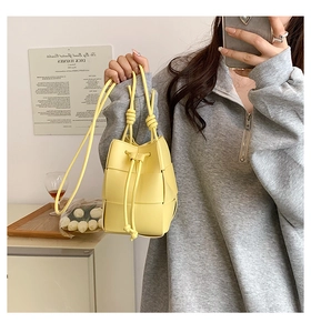 Detailed view of yellow woven bucket bag with drawstring closure and long shoulder strap