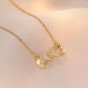 Minimalist gold infinity pendant necklace with small diamonds on soft beige fabric